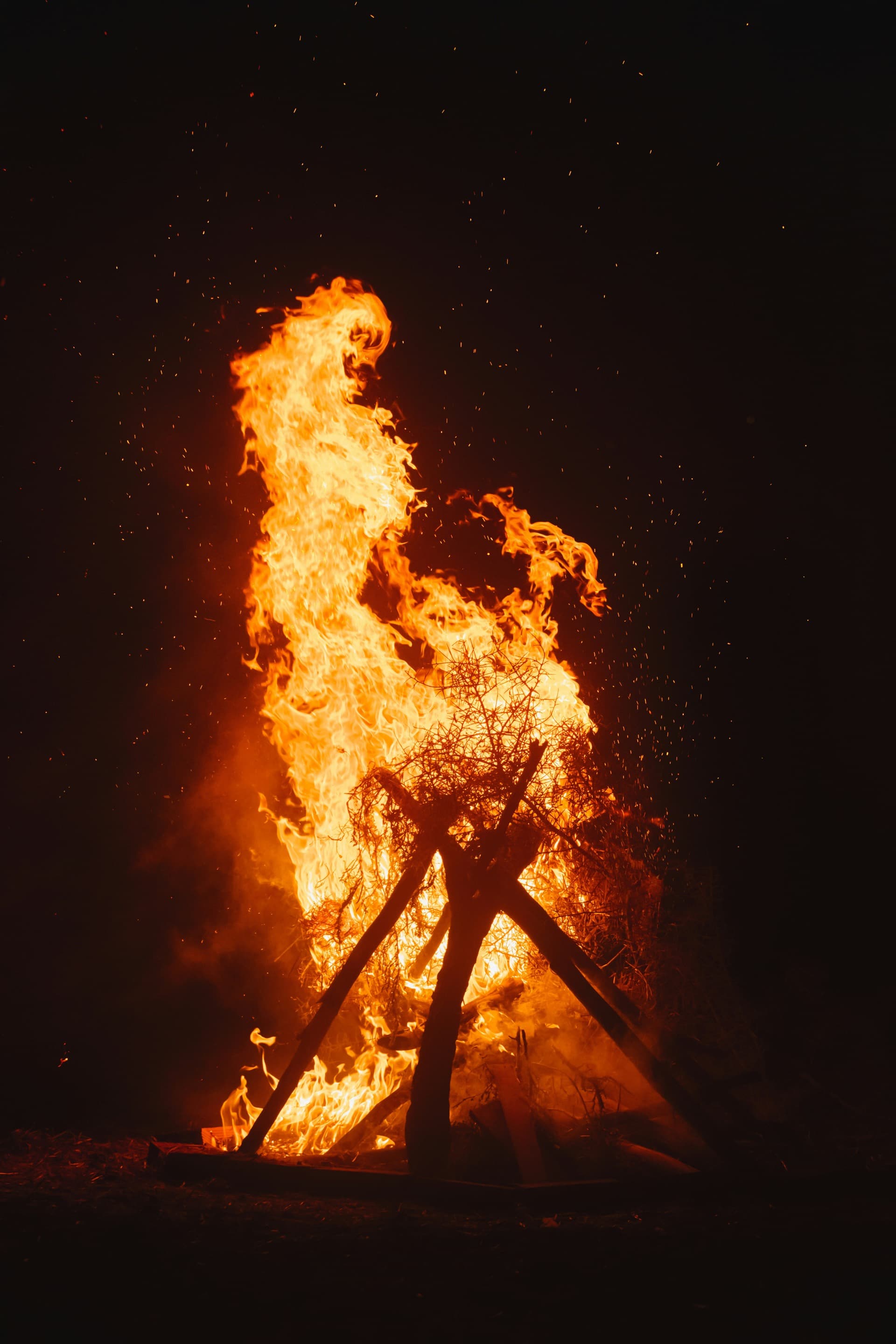 Men gathered around a large bonfire at night by a lake